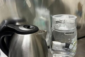 A stainless steel kettle and a clear glass with a floral pattern, both placed on a metallic surface. - Pelangi Capsule Hostel (Johor Bahru)