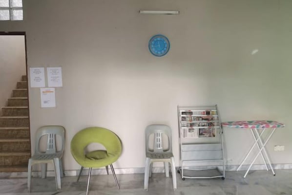 Una habitación con una escalera, dos sillas, una silla verde, una mesa con mantel y un reloj de pared.