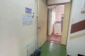 A hallway with a metal rack, a welcome sign, and a door leading to a room with a bed and a window. - Pelangi Capsule Hostel (Johor Bahru)