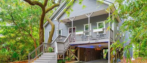 A two-story house with a covered porch, a staircase leading to the entrance, and a large tree in front.