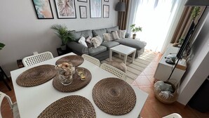 Una sala de estar moderna con un sofá gris, una mesa de comedor con individuales tejidos y cuadros en la pared.