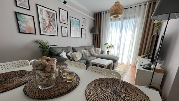 Un comedor con una mesa blanca, individuales tejidos y un florero de vidrio con piedras.
