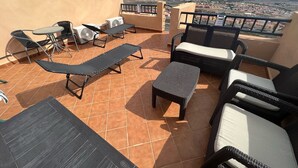 Una terraza en la azotea con mobiliario exterior, incluyendo sillones y una mesa, con vistas a la ciudad y al mar.