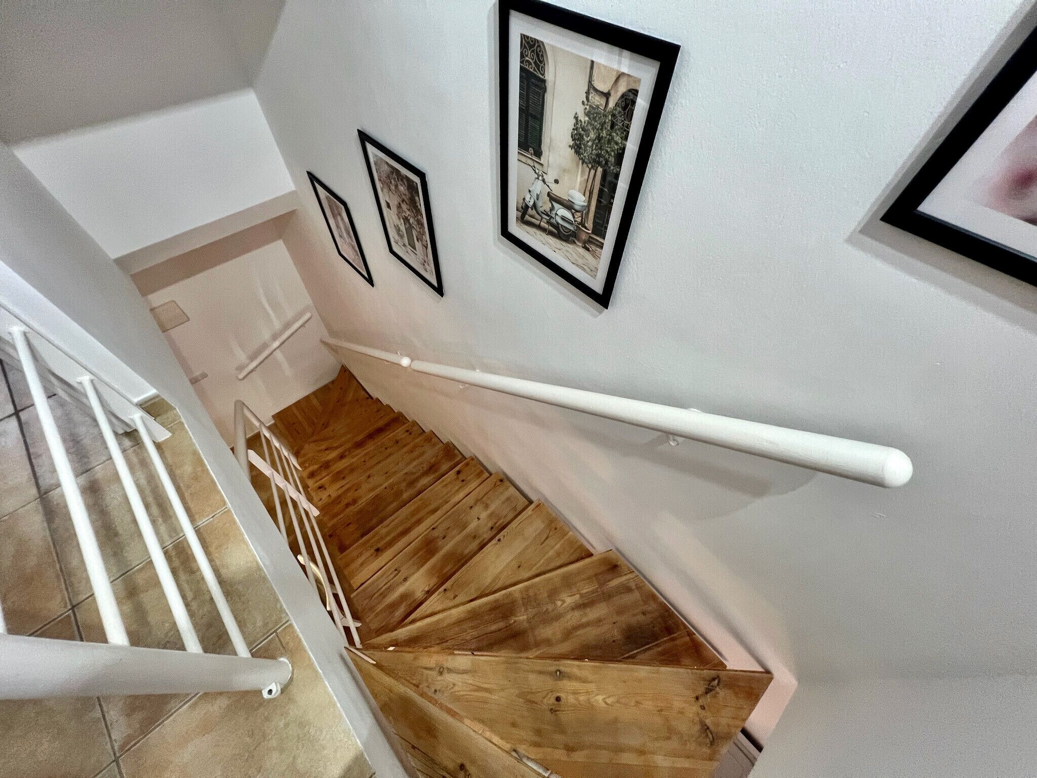 Een houten trap met witte leuningen, witte muren en wanddecoraties.