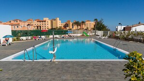 A rectangular swimming pool with a metal ladder and a safety rail, surrounded by lounge chairs and umbrellas.