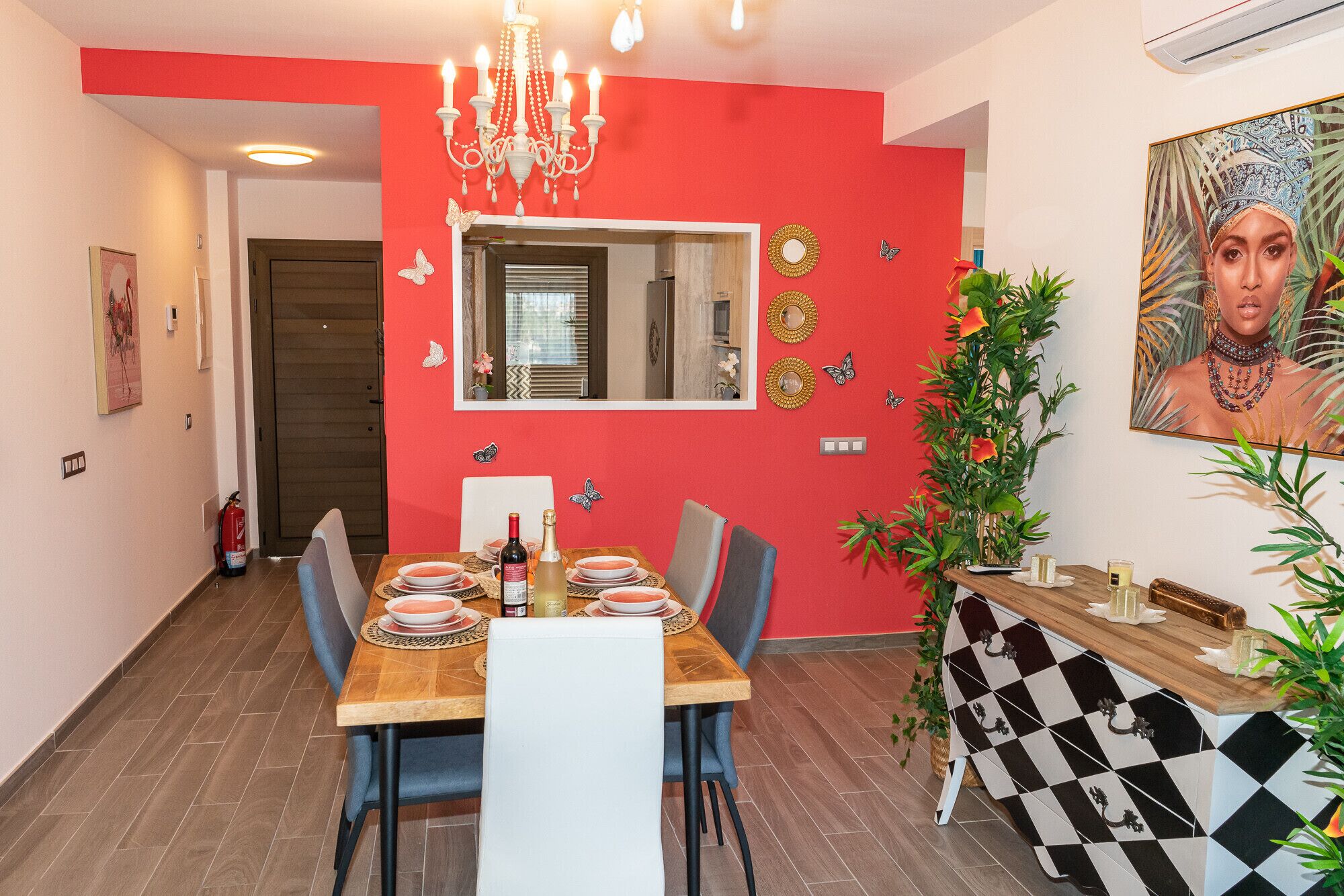 A dining area with a red accent wall, a chandelier, and a dining table set for four.