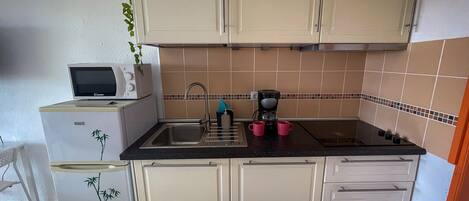 A compact kitchen with white cabinets, a black countertop, a coffee maker, and a microwave.