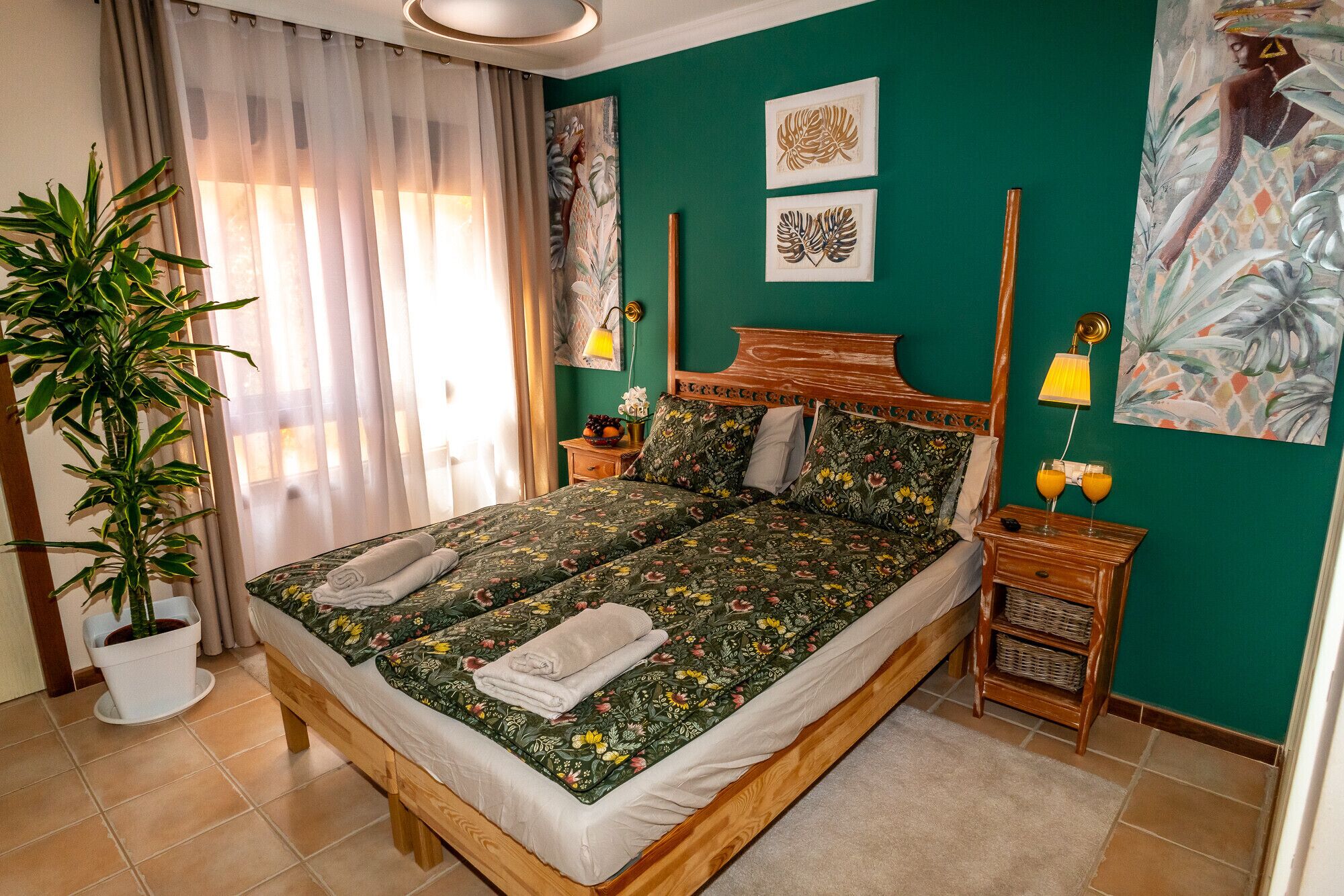 A double bed with floral bedding, a bedside table with a lamp, and a potted plant.