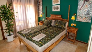 A double bed with floral bedding, a bedside table with a lamp, and a potted plant.