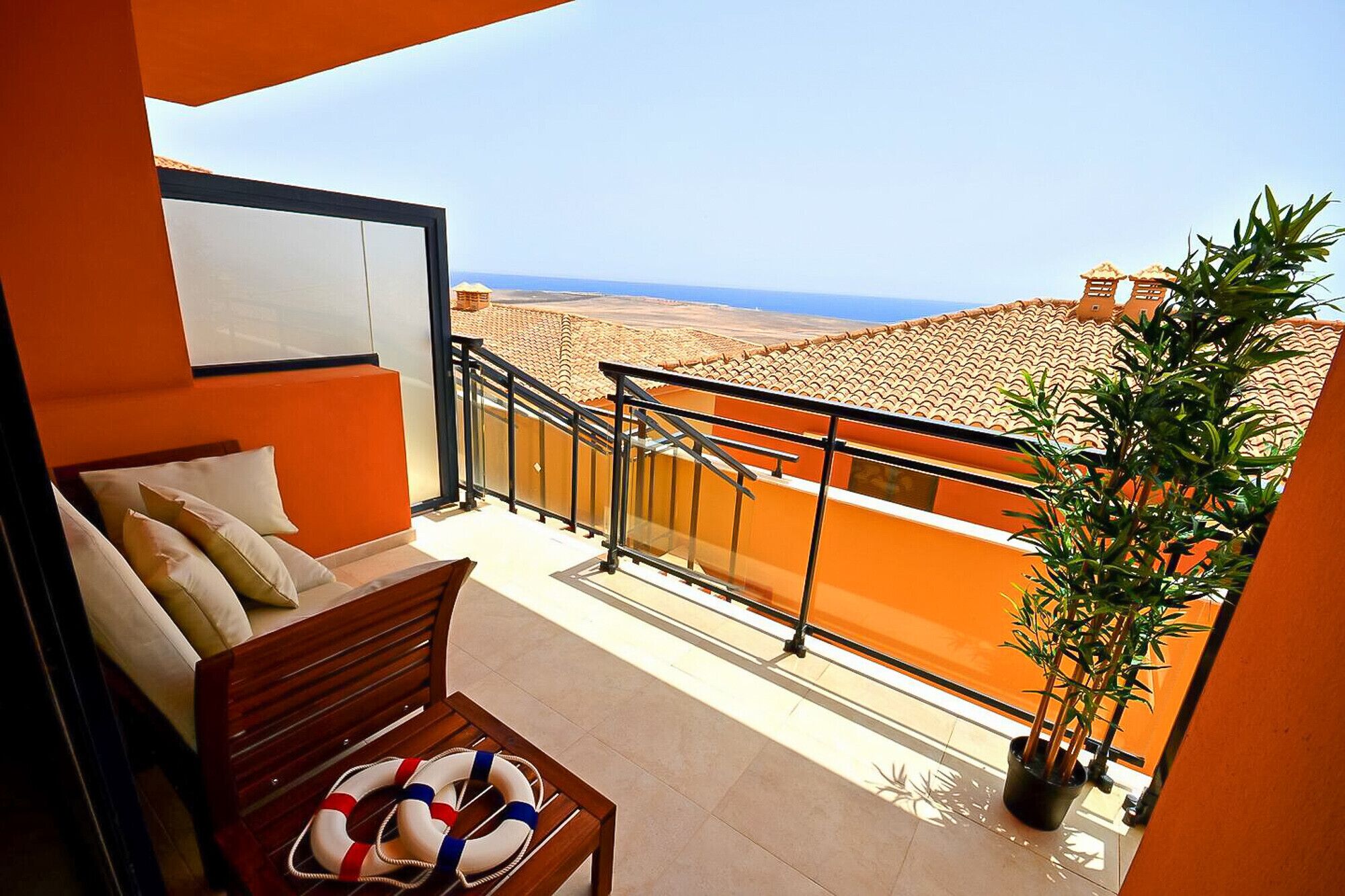 A balcony with a view of the sea, a wooden bench, a plant, and a lifebuoy.