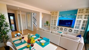 Ein modernes Wohnzimmer mit einer Couch, einem Esstisch, der für eine Mahlzeit gedeckt ist, und einem an der Wand montierten Fernseher mit blauen Akzenten.
