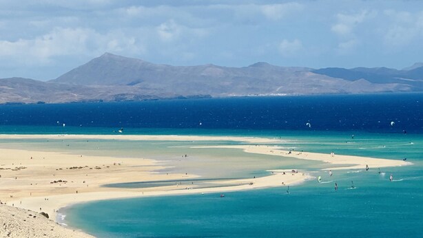 A coastal landscape with a beach, clear blue waters, and distant mountains. - Casa Garza – Castillo Mar 100m from the oceanfront (Caleta de Fuste)
