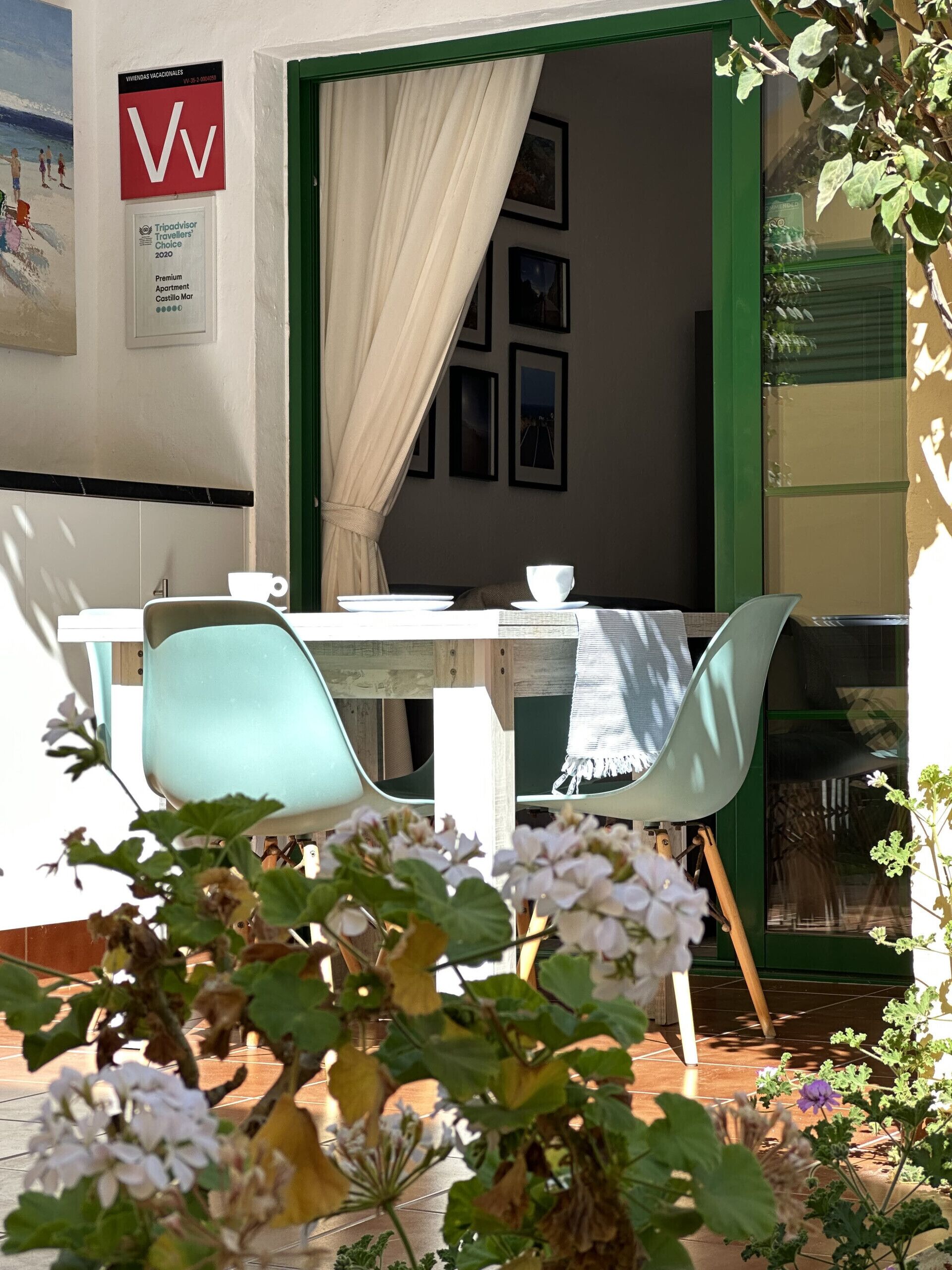 Un patio con una mesa preparada para dos, una silla y una cortina entreabierta.