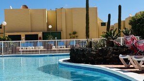 A swimming pool with lounge chairs and cacti, surrounded by a white fence and a building with a yellow facade. - Casa Garza – Castillo Mar 100m from the oceanfront (Caleta de Fuste)