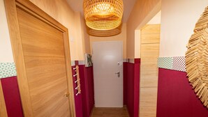 Un pasillo estrecho con puertas de madera, un papel tapiz estampado y una lámpara de fibra.