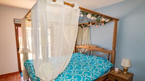 Ein Bett mit Baldachin, ein Nachttisch mit Lampe und ein floraler Schmuck am Kopfteil.