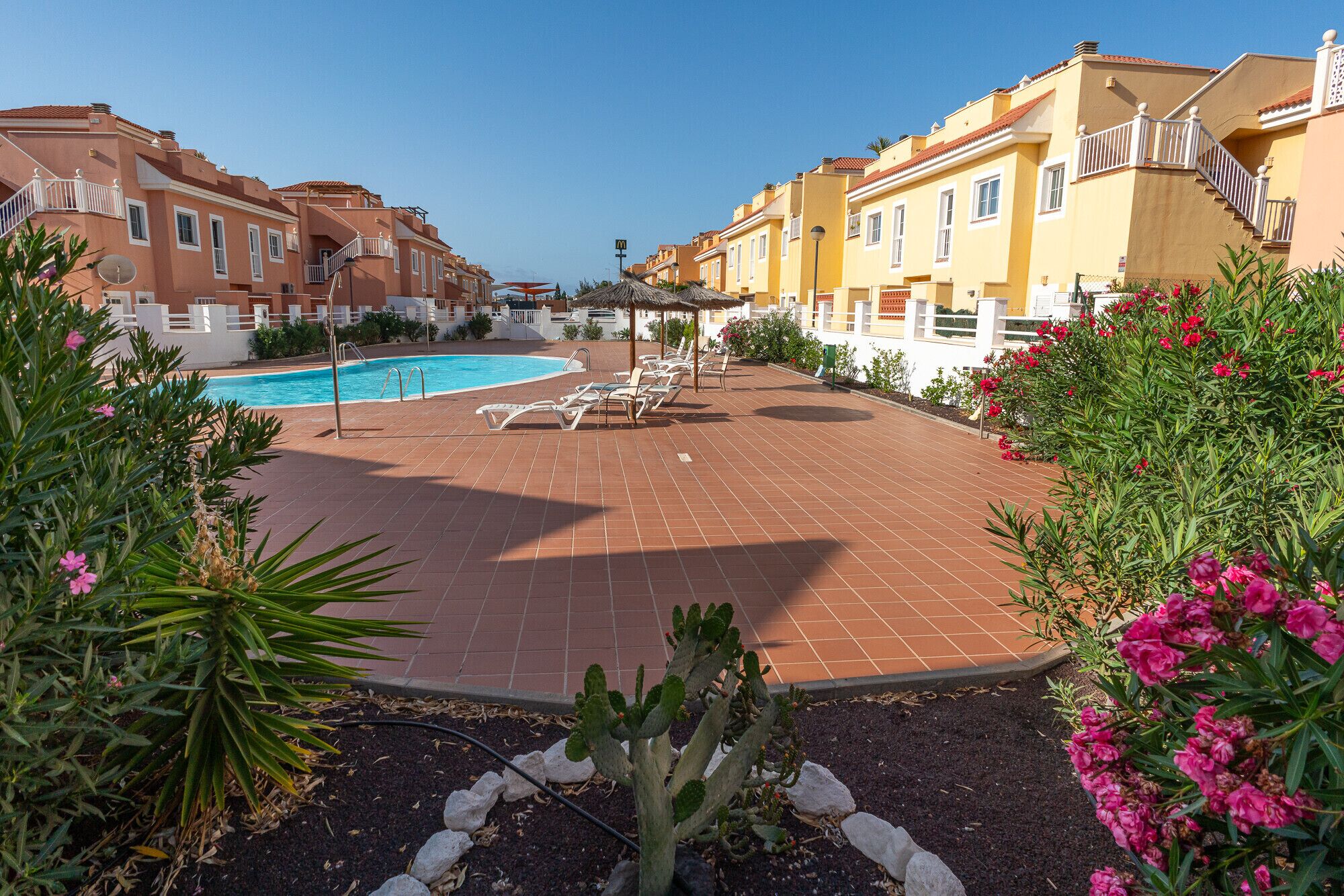 A pool area with lounge chairs and a clear blue sky.