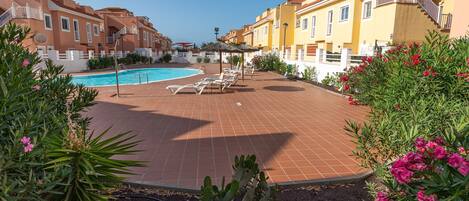 A pool area with lounge chairs and a clear blue sky.
