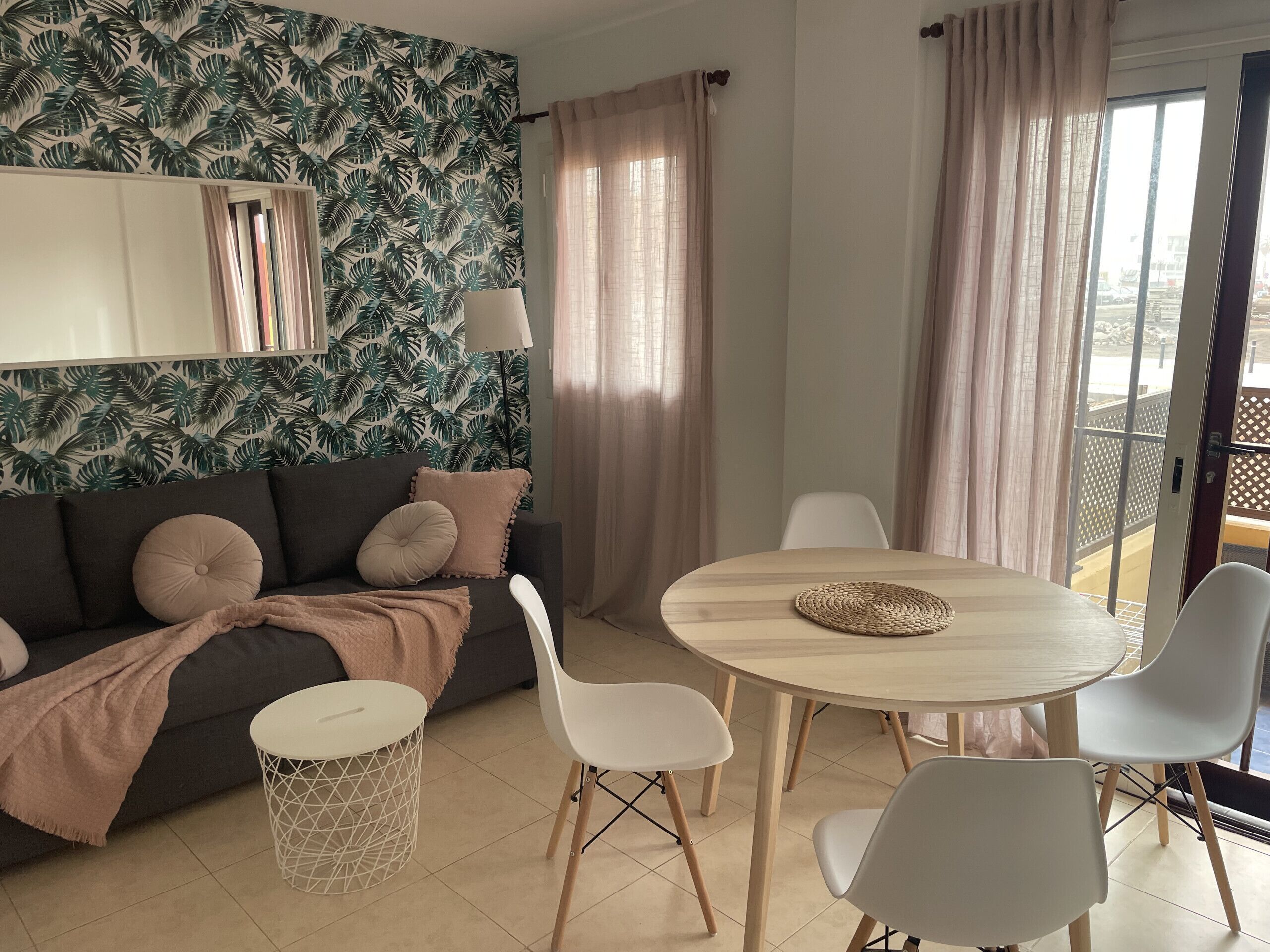 A modern living room with a dark sofa, white chairs, a round wooden table, and a patterned wallpaper.