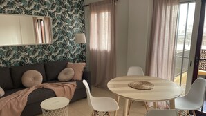 Un salon moderne avec un canapé foncé, des chaises blanches, une table ronde en bois et un papier peint à motifs.