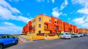 Un immeuble à plusieurs étages, doté de balcons, et un parking où sont garées plusieurs voitures.