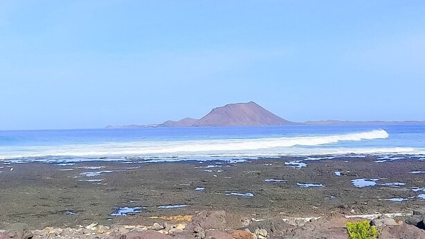 Une plage avec un rivage rocheux, des vagues qui se rapprochent du rivage et une montagne à l’horizon.
