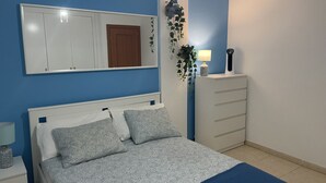 Une chambre à coucher avec un lit, une commode, un miroir et une plante fixée au mur.