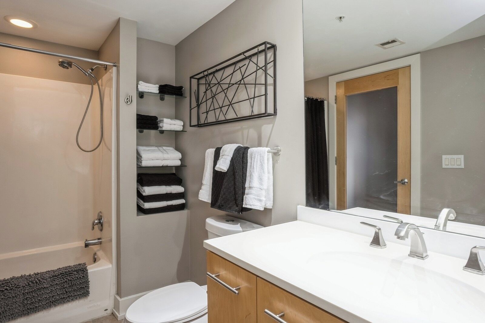 A modern bathroom with a bathtub, toilet, and a large mirror above the sink.