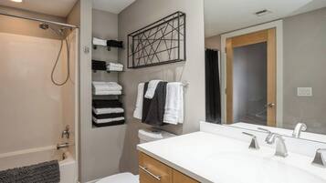 A modern bathroom with a bathtub, toilet, and a large mirror above the sink.