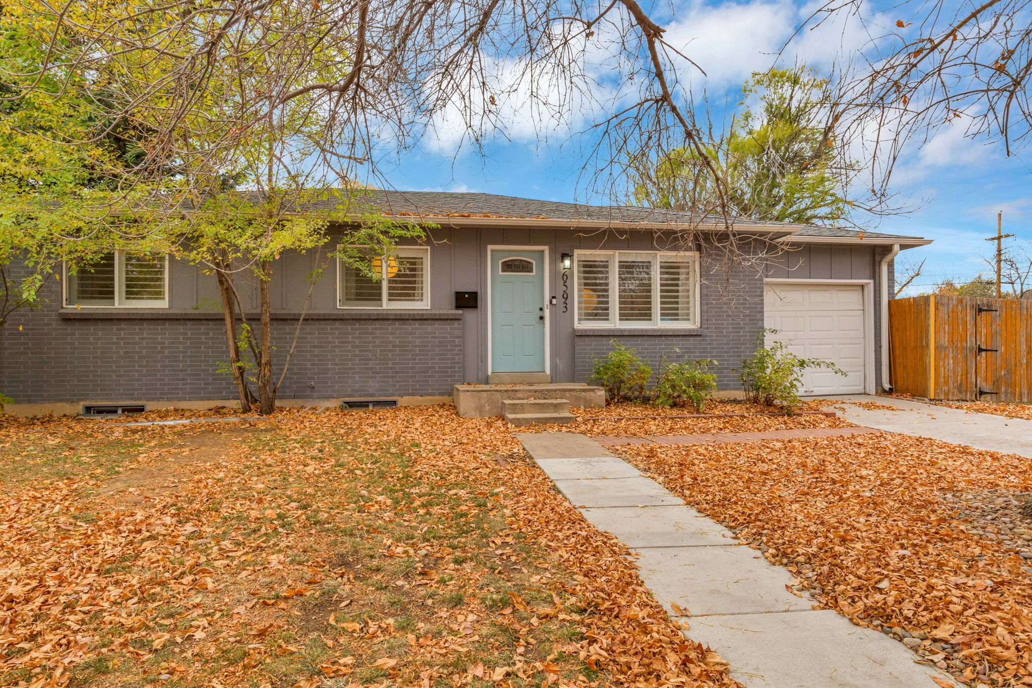 A single-story house with a front door, a garage, and a small front yard with scattered leaves.