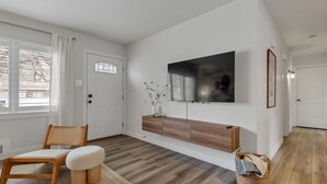 A modern living room with a wooden floor, a flat-screen TV mounted on the wall, a wooden bench, and a wicker basket. - 5BD Japanese-Themed w/ Hot Tub, Movie Room & Games (Arvada)