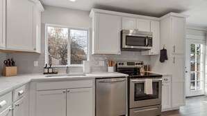 A modern kitchen with white cabinetry, stainless steel appliances, and a large window providing natural light. - 5BD Japanese-Themed w/ Hot Tub, Movie Room & Games (Arvada)