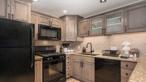 Eine moderne Küche mit Holzschränken, einem schwarzen Kühlschrank, einer Mikrowelle, einem Backofen und einem Geschirrspüler.