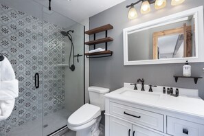 A modern bathroom with a shower, toilet, and vanity with a mirror and shelves. - Spacious 7 Bed Retreat, Hot Tub + Ski Hill Views (Fraser)