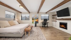 Ein modernes Schlafzimmer mit einem großen Bett, einem Schreibtisch, einem Kamin und einem an der Wand befestigten Fernseher.