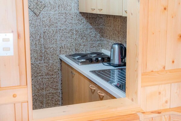 A compact kitchen with a gas stove, kettle, and wooden cabinets.
