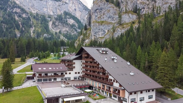 Un hotel a più piani con tetto spiovente, situato in zona montana ricca di boschi.