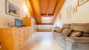 Un accogliente camera da letto mansardata con soffitto in legno, un divano, una scrivania con un computer e quadri appesi alle pareti.