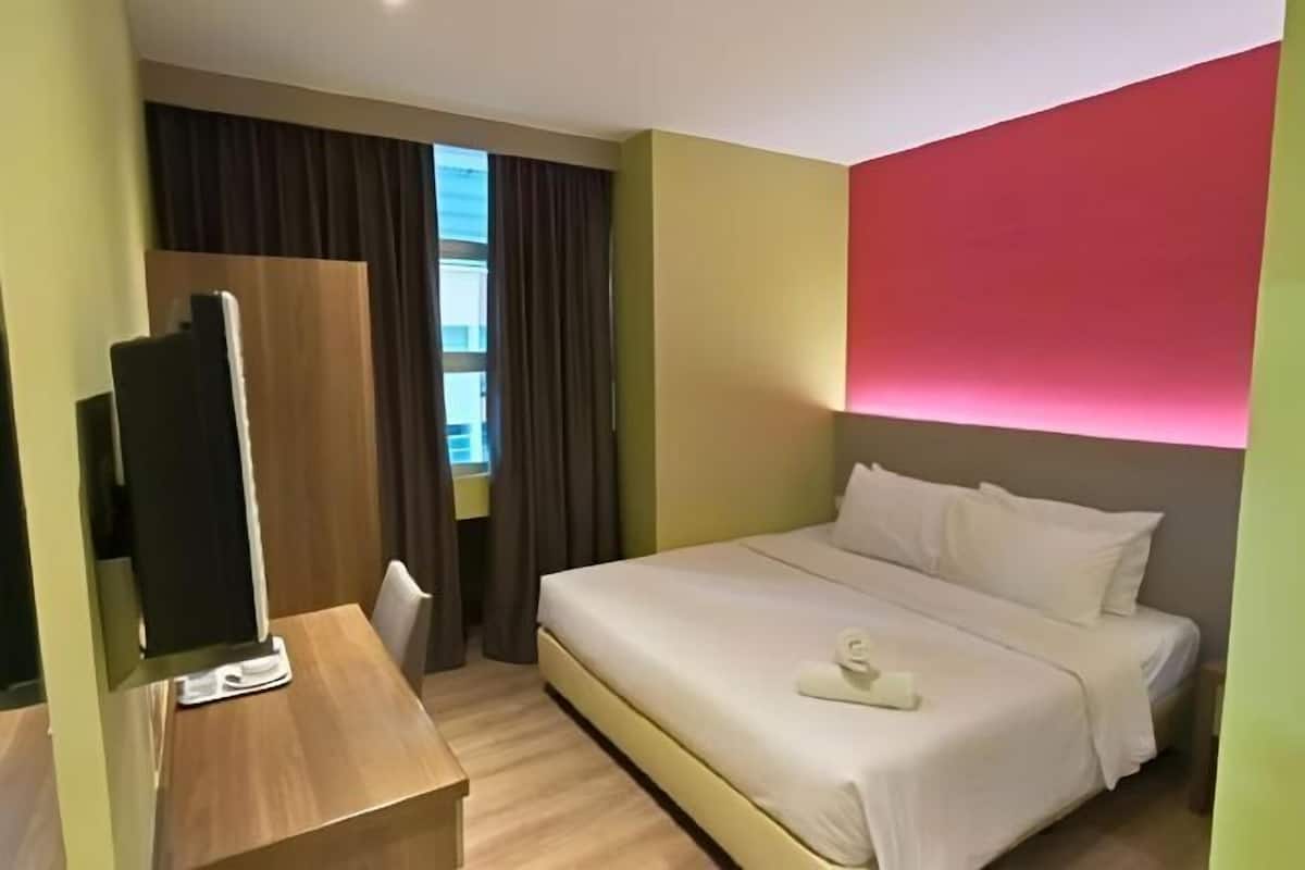 A hotel room with a bed, a desk, a TV, and a window with curtains.