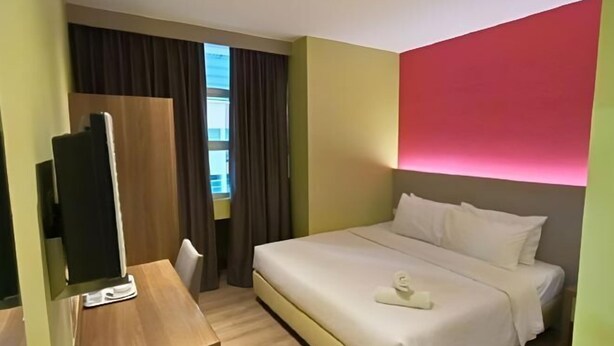 Ein Hotelzimmer mit Bett, Schreibtisch, Fernseher und einem Fenster mit Vorhängen.