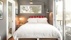 Un dormitorio con una cama grande, una ventana, una mesita de noche y cestas de mimbre.