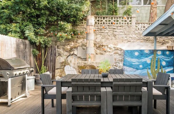 An outdoor patio with a wooden table and chairs, a barbecue grill, and a mural of a painting. - Cozy Hillside Cabin in Silverlake / Echo Park (Los Angeles)