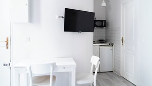 Una cocina compacta con una mesa blanca, sillas, un microondas y un televisor de pantalla plana montado en la pared.