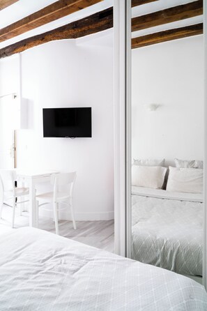 A modern bedroom with a large bed, a TV mounted on the wall, and a small desk with chairs. - Studio (1) Beaubourg - Marais - Montorgueil. (paris)