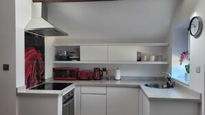 A compact kitchen with white cabinetry, a built-in oven, a microwave, a toaster, and a sink. - Beautiful Self Contained Cottages in Westbury (Trowbridge)