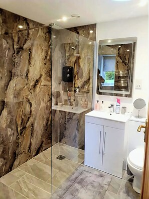 Ein modernes Badezimmer mit einer einteiligen Glasdusche, Marmorwänden, einem weißen Waschtisch mit Spiegel und einer Toilette.