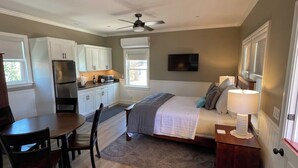 A bedroom with a bed, bedside table, lamp, and a view of the kitchen area. - Bungalow #1 by Polo House and Bungalows (Santa Ynez)