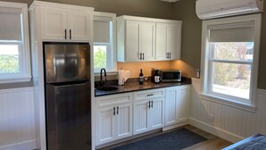 A kitchen with white cabinets, a stainless steel refrigerator, a microwave, and a window with a view of greenery. - Bungalow #1 by Polo House and Bungalows (Santa Ynez)
