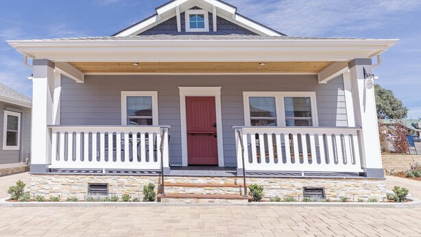 A two-story house with a red door, white railings, and a stone foundation. - Bungalow #1 by Polo House and Bungalows (Santa Ynez)