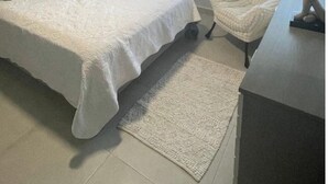 Een slaapkamer met een bed, een stoel, een bureau, een plafondventilator en een raam met jaloezieën.